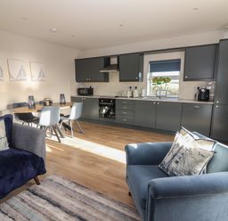 A kitchen and dining area with dark cabinets a dining table with four chairs and two armchairs at The Boathouse in Carrigaholt County Clare