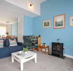A living room with a blue sofa, green armchair, white coffee table, small fireplace, and framed pictures on a blue wall at Waters Edge Ymyl Y Dwr in Y Felinheli
