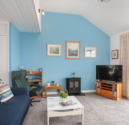 A living room with a blue wall sofa armchair coffee table and television at Waters Edge Ymyl Y Dwr in Y Felinheli