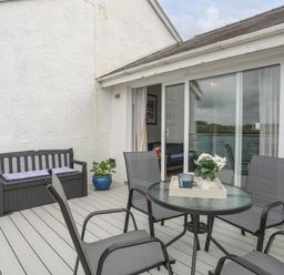 A patio with a round glass table and four chairs and a bench with cushions at Waters Edge Ymyl Y Dwr in Y Felinheli