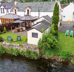 A riverside garden with outdoor seating and a patio next to a row of white cottages at River Cottage in Eamont Bridge