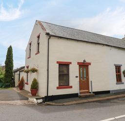 A street view of a connected two story and one story house with potted plants and hanging flower baskets at River Cottage in Eamont Bridge