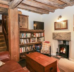 A living room with wooden ceiling beams a bookshelf a fireplace and a wooden chest at Eden Vale in Broughton-In-Furness