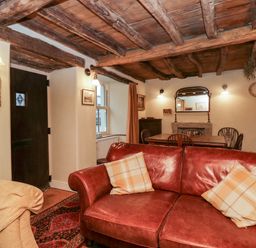 A living room with a red sofa, a wooden dining table, chairs, a mirror above a fireplace, and wooden ceiling beams at Eden Vale in Broughton-In-Furness