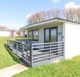 A single-story cottage with a fenced porch and outdoor seating on a grassy area at Cassia in Kilkhampton