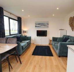 A living room with a sofa, television, and dining table at Cassia in Kilkhampton