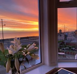 A view of a sunset over the sea through a window with white lilies on the windowsill at 46 The Promenade in Withernsea