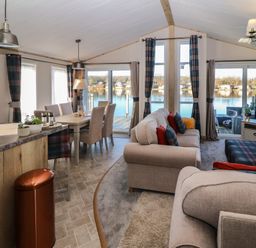 A living and dining area with sofas dining table chairs and windows overlooking a lake at Gressingham 7 in Warton near Carnforth