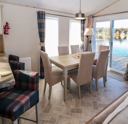 A dining room with a rectangular wooden table six upholstered chairs and stools by a kitchen counter at Gressingham 7 in Warton near Carnforth