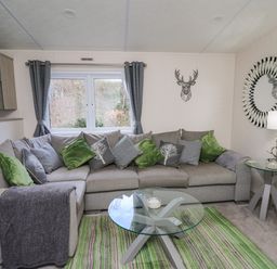 A living room with a sectional sofa with green and gray cushions and two glass tables at 43 The Deri in Llanarth
