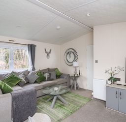 A living room with a large sofa with green and patterned cushions a glass coffee table and a television at 43 The Deri in Llanarth