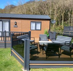 A patio area with outdoor seating and table next to a wooden cabin surrounded by trees at 43 The Deri in Llanarth