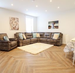 A living room with a large sectional sofa and recliner chairs a white rug and two animal paintings at Gwydyr Bach 1 in Llanrwst