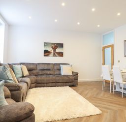 A living room with a grey sectional sofa, blue and beige pillows, a white fluffy rug, a dining table with white chairs, and an elephant painting on the wall at Gwydyr Bach 1 in Llanrwst
