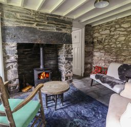 A room with stone walls a wood burning stove two armchairs a small wooden table and a couch with a fur throw at Nyth Yr Eryr in Blaenau Ffestiniog