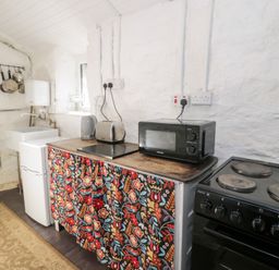 A kitchen with a small fridge a sink a toaster kettle microwave and stove with a floral curtain below the counter at Nyth Yr Eryr in Blaenau Ffestiniog