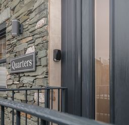 Stone wall with a window and a sign reading Quarters next to a dark colored door at Quarters in Ambleside