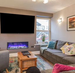 A living room with a gray sofa and colorful cushions a wooden coffee table a wall-mounted television and an electric fireplace at Quarters in Ambleside