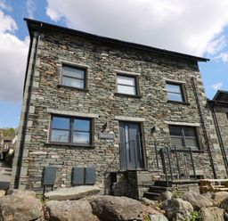 A stone building with multiple windows and a door with steps at Quarters in Ambleside