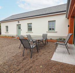 An outdoor patio area with a glass table and six chairs outside a white building with green windows at Curhoor Near Loughrea County Galway