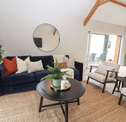 A living room with a navy sofa with cushions a round mirror above a black coffee table with plants and candles two beige armchairs a sliding glass door and wooden ceiling beams at Curhoor Near Loughrea County Galway