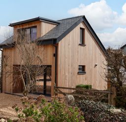 A wooden house with black trim and a gravel yard with leafless trees at The Cabin at Ropewalk in Goonbell near St Agnes