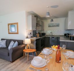 A kitchen and dining area with a gray couch and table set for four at 14 Coedrath Park in Saundersfoot