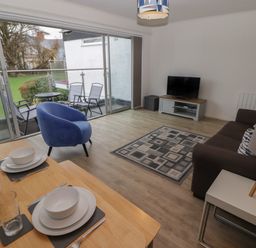A living room with a sofa a blue chair a dining table set near sliding glass doors leading to a balcony at 19 Coedrath Park in Saundersfoot