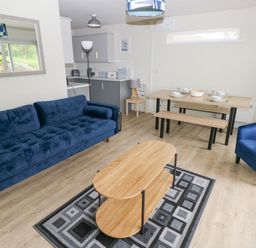 A living room with a blue sofa, blue armchair, wooden coffee table on a patterned rug, and a dining table with benches at 29 Coedrath Park Saundersfoot