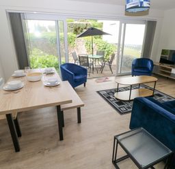 A living room with blue sofas and chairs a wooden dining table set with dishes and glassware and a TV on a stand at 29 Coedrath Park Saundersfoot