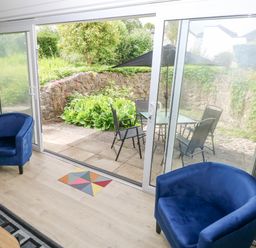 A room with two blue armchairs facing glass sliding doors leading to a patio with a table and chairs at 29 Coedrath Park in Saundersfoot