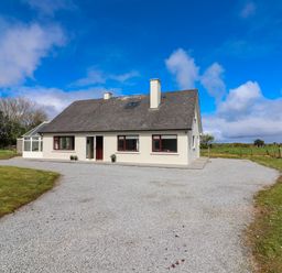 A single story house with a gray roof and white walls surrounded by gravel and grass at Tonakilla House in Tonakilly near Camp County Kerry