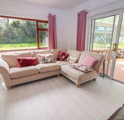 A beige corner sofa with cushions in front of large windows and sliding glass doors at Tonakilla House Tonakilly near Camp County Kerry