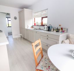 A kitchen with white cabinets a wooden chair with floral cushion a white round table and various kitchen appliances at Tonakilla House in Tonakilly near Camp County Kerry