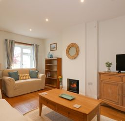 A living room with two sofas a wooden coffee table a bookshelf a TV on a cabinet and a small fireplace at Sea Breeze in Swanage