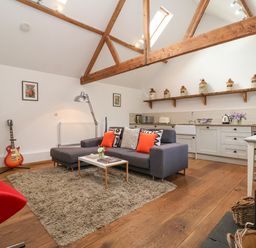 An open living room and kitchen with wooden beams a gray sofa with orange cushions a guitar and a red chair at The Nook in Chediston near Halesworth