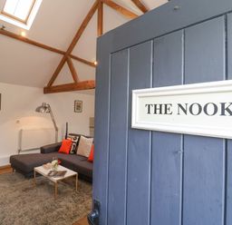 A seating area with a gray sofa orange cushions coffee table and a guitar near a lamp at The Nook in Chediston near Halesworth