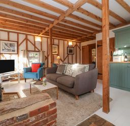 A living room with a grey sofa blue armchair white coffee table and green kitchen cabinets at Twosome in Chediston near Halesworth