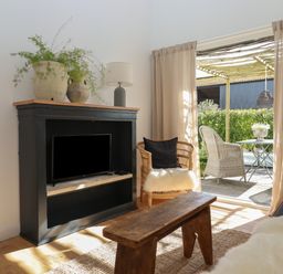 A living room with a black TV cabinet holding a TV and lamps beside a chair and wooden bench by a sliding door at The Apple Shed in Upexe near Silverton