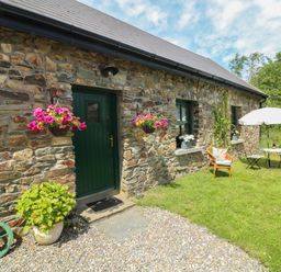 A stone house with a green door two hanging flower baskets and outdoor seating with an umbrella at Bohan Bo in Tinteskin near Kilmuckridge County Wexford