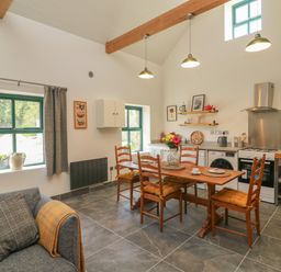 A kitchen with wooden dining table and chairs a couch by the window and cooking appliances at Bohan Bo in Tinteskin near Kilmuckridge County Wexford