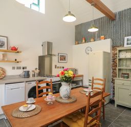 A kitchen with wooden dining table and chairs a vase with flowers a refrigerator and shelves with cups and plates at Bohan Bo in Tinteskin near Kilmuckridge County Wexford