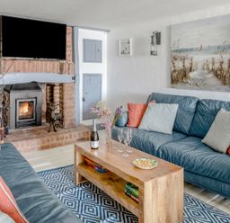 A living room with blue sofas a wooden coffee table a fireplace and a mounted TV at The Cubby Hole in Sennen Cove