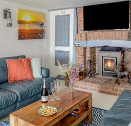 A living room with two leather sofas a wooden coffee table and a brick fireplace with a television above at The Cubby Hole in Sennen Cove