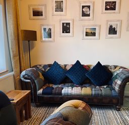 A living room with a patchwork sofa with three blue cushions a wooden side table and framed pictures on the wall at Harvest Moon Cottage in Much Cowarne