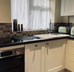 A kitchen with white cabinets black countertop a stove oven sink toaster kettle and three decorative containers on the windowsill at Harvest Moon Cottage in Much Cowarne