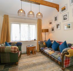 A living room with two patchwork sofas with blue cushions a floor lamp and framed pictures on the wall at Harvest Moon Cottage in Much Cowarne