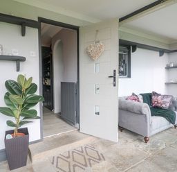 An open door leading into a room with a grey armchair with floral pillows a potted plant near the door shelves on the walls and a stone floor at The Lodge at Wildersley Farm in Belper