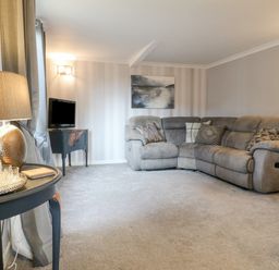 A living room with a gray sectional sofa and a small TV on a stand at The Lodge at Wildersley Farm in Belper