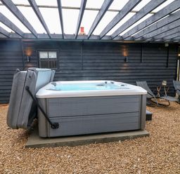 An outdoor covered area with a hot tub and two lounge chairs at The Lodge at Wildersley Farm in Belper